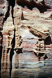 Photographie d'un ancien monument sculpté dans la roche. Le monument est dégradé par les intempéries et donne l’impression de se fondre dans la roche.