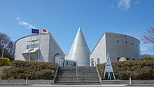 Photographie couleur d'un bâtiment moderne avec des drapeaux flottants au vent.