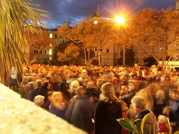 A crowd on ANZAC Day next to the Wellington cenotaph with the sun rising over the Old Government Building