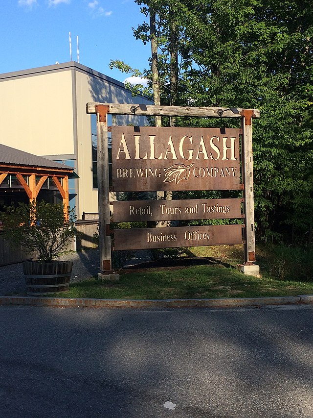 This is the welcome sign to the Allagash Brewery in Portland Maine. The sign is made of wood and has "Allagash Brewing Company. Retails, Tours, and Tastings. Business Offices," engraved onto it. The photo was taken in 2017 and it is possible that the exterior has since changed.