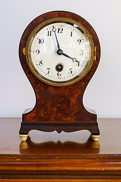 Clock with enamel face in round wooden housing, presumably walnut