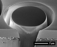 An electron microscope image of an approximately 13 micrometre piece of dielectric mirror being cut from a larger substrate. Alternating layers of Ta2O5 and SiO2 are visible on the bottom edge. DBR SEM.jpg