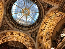 Photo montrant le plafond de la salle en forme de dôme.  Le plafond est finement décoré avec le dôme en verre et les détails dorés sur les arches.