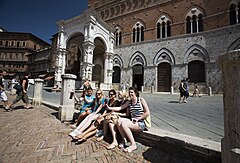 group of young women on holiday in front of Campanile or Siena Tower view in Piazza del campo, the main square Siena, Italy