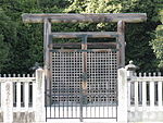 Wooden torii gate. And concrete fence in front of trees.