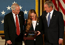 Ein Farbbild von Murphys Eltern, die neben Präsident George Bush vor einer amerikanischen Flagge stehen.  Sie halten Murphys Ehrenmedaille in einer Vitrine und schauen darauf hinab.