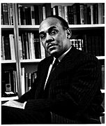 Photograph of Ralph Ellison, seated, with bookshelves behind him