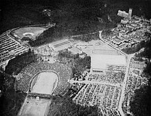 Aerial photo from game day of Duke Stadium, a horseshoe-shaped football venue, and the surrounding area of Duke's West Campus. The stadium is packed with fans, including the temporary extra bleachers that have been installed in the open end of the horseshoe as well as around the top rim of the stadium. There are uncountably many cars parked in lots around the stadium taking more area than the stadium itself. The main area of West Campus with Gothic Revival architecture, including Duke Chapel, as well as the basketball and baseball venues are visible, and are all surrounded by dense woods.