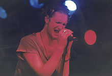 Un cantante maschio, Layne Staley, si esibisce sul palco con Alice in Chains.  Tiene il microfono con entrambe le mani e i suoi occhi sono chiusi mentre canta.