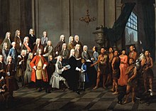 Yamacraw Native Americans meet with the trustee of the colonial-era Province of Georgia in England in July 1734, depicted in a portrait showing a Native American boy (in blue coat) and woman (in red dress) in European clothing; the portrait includes James Oglethorpe, the British founder of the Province of Georgia, and Tomochichi, chief of the Yamacraw tribe. Tomo-chi-chi and other Yamacraws Native Americans.jpg