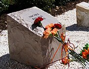 A photo of one of the commemorative stones at the memorial with flowers laid on top of it.