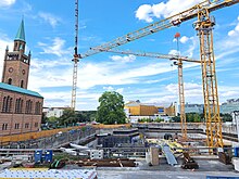 Es ist eine große Baugrube zu sehen, mehrere Kräne und eine Kirche.