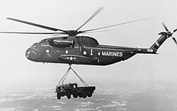 Black and white photograph of a helicopter in flight with a truck slung below it