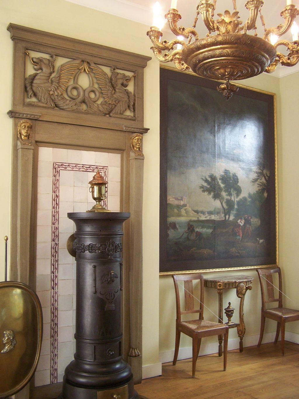An example of Directoire style with a large painting on the right, a gold chandelier and two tan chairs. 