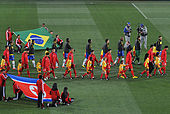 Deux équipes (en rouge et en jaune) entrent sur un terrain de football, accompagnés d'enfants.