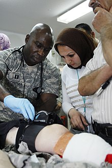 Captain Ernest Dorema, an officer in charge of the emergency room at the 28th Combat Support Hospital shows Sinna Abdul Azeez, an anesthesiologist with Yarmouk Hospital, how to use a Combat Application Tourniquet on the leg of a mock casualty during an exercise as a part of Operation Medical Alliance held at Sather Air Base, 7 April 2007. Flickr - The U.S. Army - Combat hospital staff welcomes Iraqi doctors during medical information exchange program.jpg