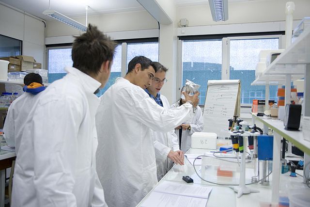 Scienca studento, kunportante blankan laborveston, observas atente pesujon en laboratorio.