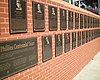 A succession of black metal plaques mounted on a brick wall. In the foreground is one plaque larger than the other entitled "Phillies Centennial Team". The smaller plaques each have a face and inscribed text.