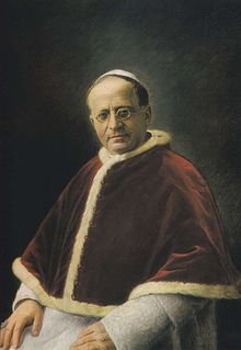 Portrait d'un homme portant des lunettes, coiffé d'une calotte blanche et portant une soutane blanche et une mosette rouge.