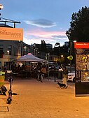 People on a street in the sunset under some gazebos and person walking a dog