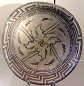 Samarra plate, with a design consists of a rim, a circle of eight fish, and four fish swimming towards the center being caught by four birds, at the center being a swastika symbol; circa 4000 BCE; painted ceramic; diameter: 27.7 cm; Vorderasiatisches Museum (Berlin)