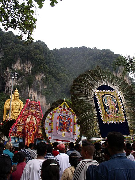 Icons carried in procession during Thaipusam at Batu Caves. Also seen in the background is the 42.7 m high golden statue of Lord Murugan.