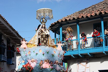 A saqra (animal figure) dancer watching the procession of Mamacha Carmen from a balcony