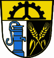 Gemeinde Holenbrunn Unter goldenem Schildhaupt, darin ein oberhalbes schwarzes Zahnrad, gespalten von Silber und Schwarz; vorne ein wachsender blauer Pumpbrunnen, hinten schräg gekreuzt zwei goldene Ähren.