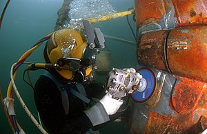 Водолаз в водолазном шлеме шлифует заплатку на подводной лодке