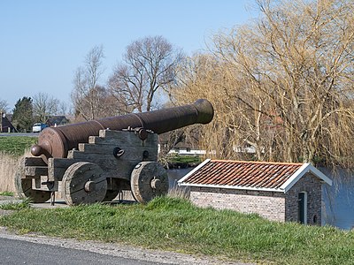 High water alarm cannon on the dike near Blankenham. The building at the bottom of the dike is a gunpowder storage. The pond in the background is the result of a dike breach. The eroding water made it very deep so the repaired dike was build around it. There are many such ponds to be found on the dike near Blankenham.