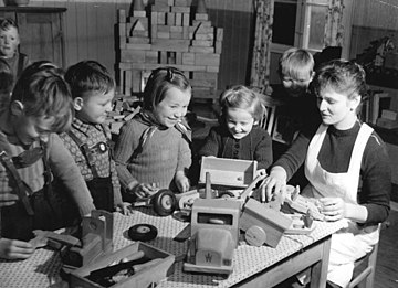 Four kindergarten children play with toy trucks on a table and a teacher sits with them while they play