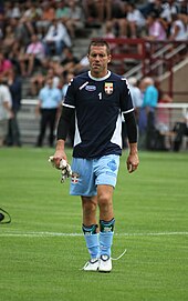 Foto waarop Johann Durand te zien is in blauw trainingspak en shirt nummer één met een paar voetbal keepershandschoenen in zijn rechterhand