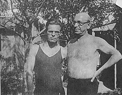 Photograph of Nestor Makhno and Alexander Berkman standing together, Makhno wearing a vest and glasses, Berkman shirtless and wearing glasses