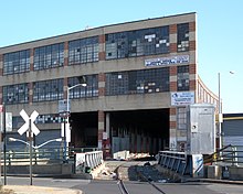 Il Bushwick Branch, una ferrovia a binario unico, attraversa Flushing Avenue su un ponte e poi entra nel Maspeth Industrial Center, un edificio industriale