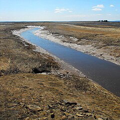 Missiguash River at low tide, spring 2009. Nova Scotia to left.  In the background is the National Historic Site of Tonges Island, former home in 1676 of the Seigneur Michel de la Valliere, governor of Acadia.