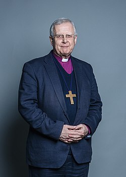 Donald Allister stående, i mörkt grå kavaj, kors om halsen, purpurfärgad biskopsskjorta.