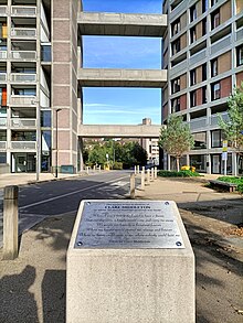 A silver plaque mounted on a concrete pillar, with a dedication to and a poem written by Clare Middleton. In the background, the I Love You sign is visible.