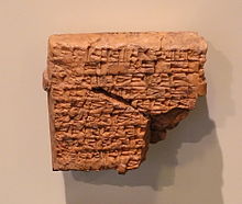 Tablilla cuadrada de material rojo, rota en ángulo e inscrita con signos cuneiformes.