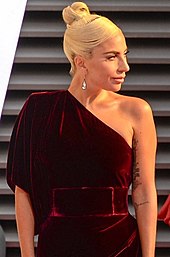 Uma foto de Lady Gaga em um vestido bordô de um ombro só, olhando para a direita.