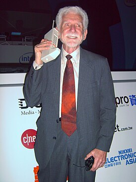 Amerykański inżynier Martin Cooper w 2007 roku.  W rękach jednego z pierwszych modeli telefonów komórkowych.