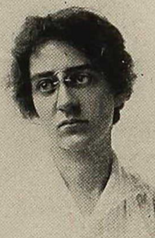 A young white woman with short dark hair, wearing glasses and a white blouse
