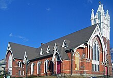 Batu bata gereja, dilihat dari sudut dan terlihat menanjak, dengan tinggi menara putih. Salah satu jendela depan telah naik.