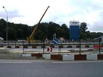 Вид на строительную площадку с чётной стороны улицы Дыбенко. На фоне будущей станции виден Химкинский лесопарк. Июль 2015 года