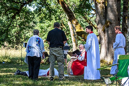 In an outdoor Anglican ordination service, a deacon being ordained to the priesthood prostrates himself before the seated bishop.