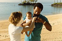 Een man en een vrouw die een jong kind vasthouden op een paradijselijk strand.