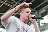 Prof in a white t-shirt holding a microphone to his lips with one hand