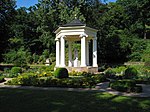 Heutige Ansicht des im Jahre 1803 errichteten Musentempels mit einer Polyhymnia-Skulptur im Zentrum sowie aufwendiger Schmuckbepflanzung rund um die Parkarchitektur herum.