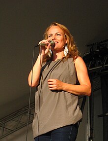 Woman holding microphone while squinting into the sun