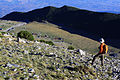 A hiker stands above Novosella huts under Rusolia peak