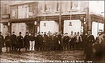 Residents standing in front of boarded-up shops damaged during the evening of November 8, 1910, known as the Tonypandy Riots, in Tonypandy, Rhondda, Wales. Tonypandy Riots 1910.jpeg